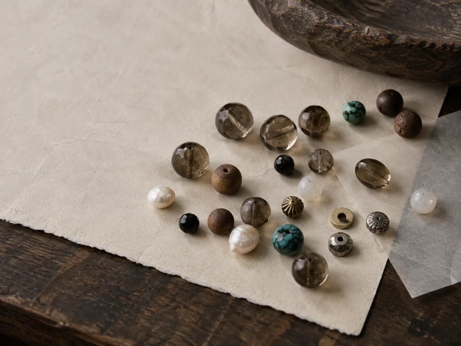 Loose smoky quartz, wood, pearl, moonstone, black spinel, turquoise, brass, and silver bracelet components on a studio table.