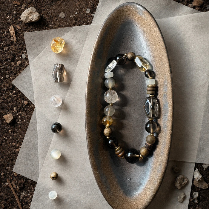 Strata Afterglow Bracelet styled on a dark ceramic dish with smoky quartz, moonstone, citrine, sandalwood, and brass details