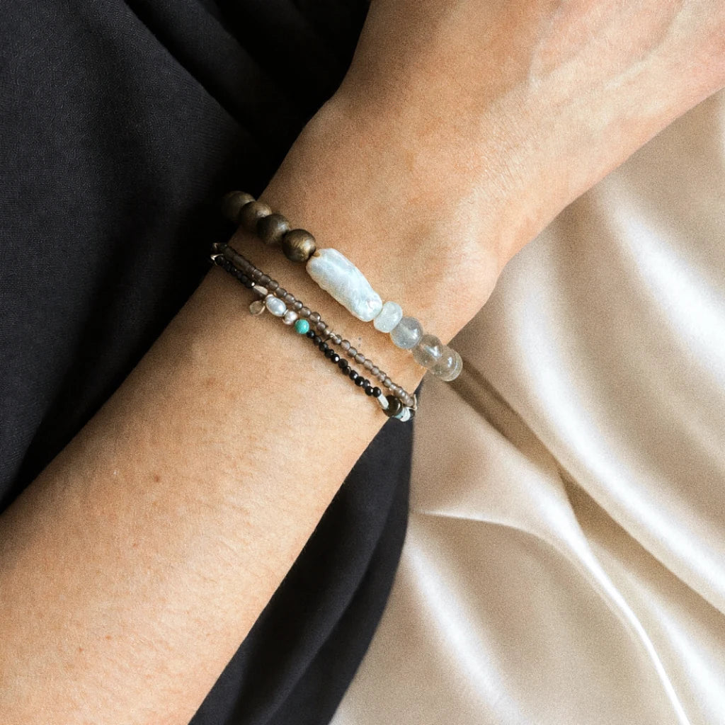Strata Pale Drift Bracelet worn on the wrist, showing its smoky quartz, pearl, moonstone, and agarwood composition