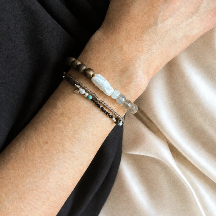 Strata Pale Drift Bracelet worn on the wrist, showing its smoky quartz, pearl, moonstone, and agarwood composition