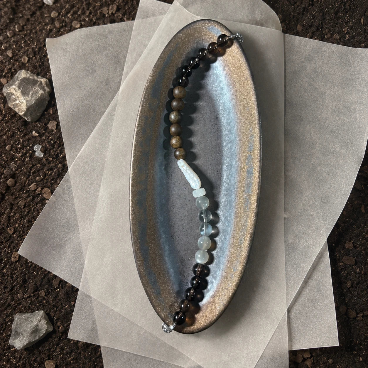 Strata Pale Drift Bracelet styled on a dark surface with pearl, moonstone, smoky quartz, and agarwood details
