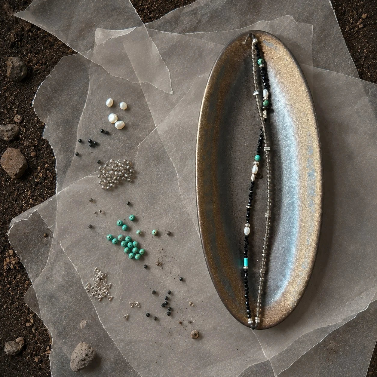 Strata Still Current Bracelet styled on a dark ceramic dish with black spinel, smoky quartz, turquoise, pearl, and silver details
