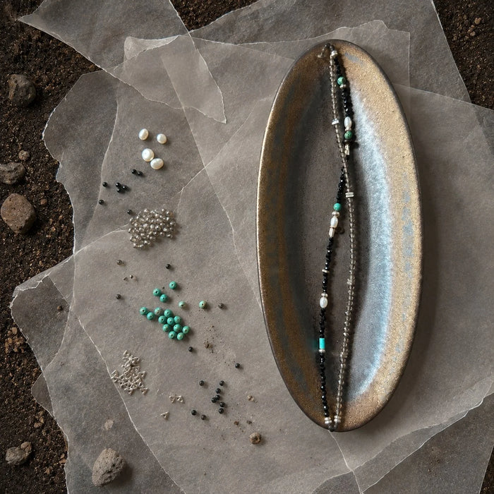 Strata Still Current Bracelet styled on a dark ceramic dish with black spinel, smoky quartz, turquoise, pearl, and silver details