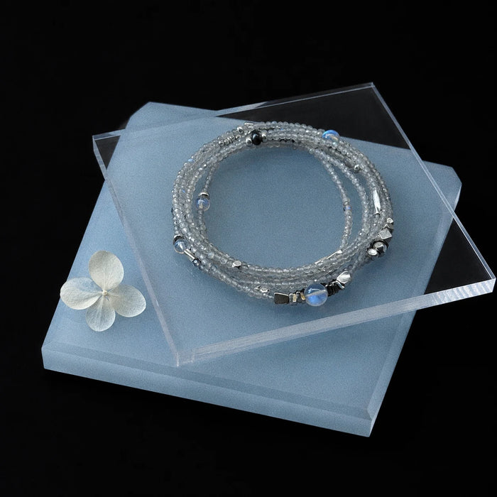 Veiled Light Moon Dust Bracelet styled on pale blue acrylic with layered grey moonstone strands and silver accents