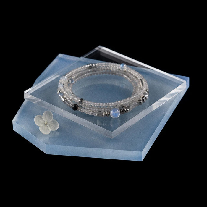 Veiled Light Moon Dust Bracelet arranged on translucent blue displays with moonstone, obsidian, and silver details
