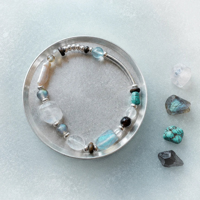 Veiled Light Prism Bracelet on a pale blue surface beside moonstone, labradorite, turquoise, and obsidian stones