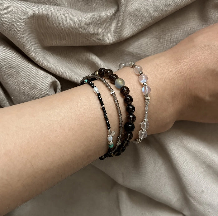 Veiled Light Trace Bracelet layered with darker bracelets for a mixed-texture wrist styling look